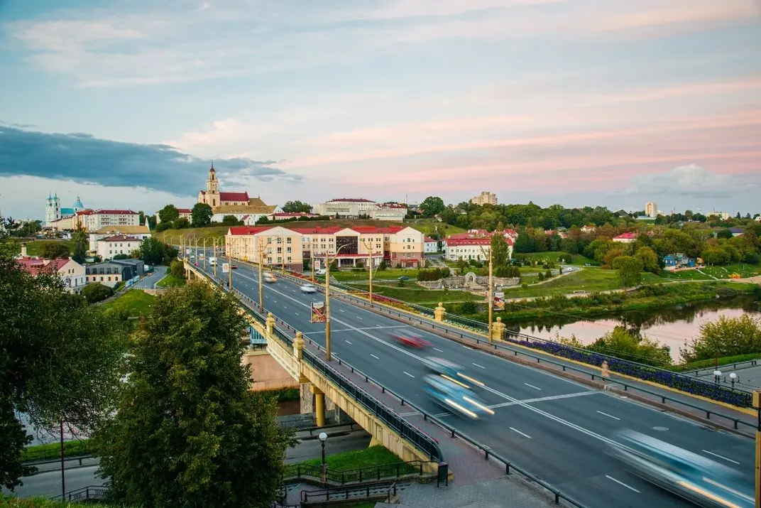Автомобили проезжают по мосту в Гродно на закате с видом на город