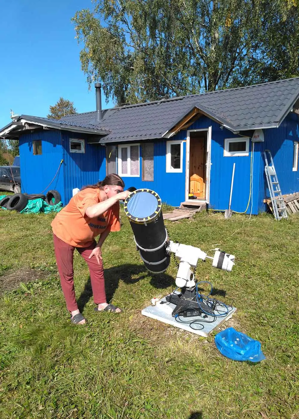 Мужчина смотрит в телескоп днем на фоне деревянного домика