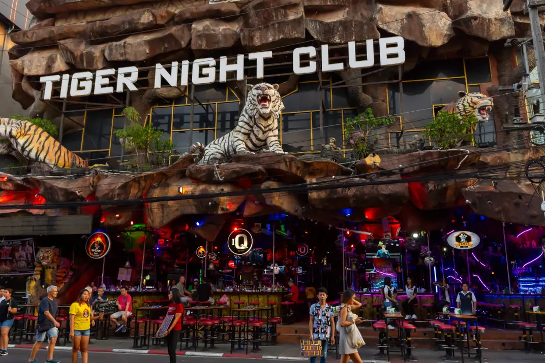 Люди идут мимо фасада клуба Tiger Night Club, на котором размещены скульптурные фигуры тигров, Патонг