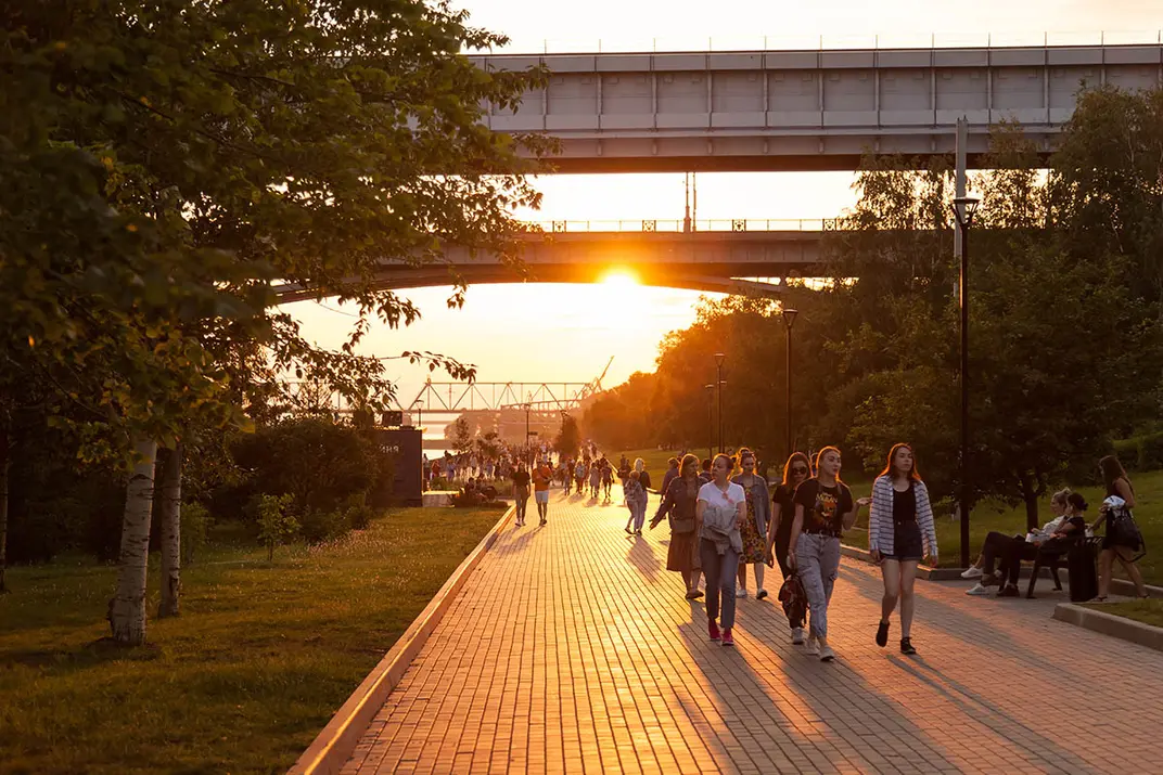 Люди гуляют на закате в парке на фоне моста