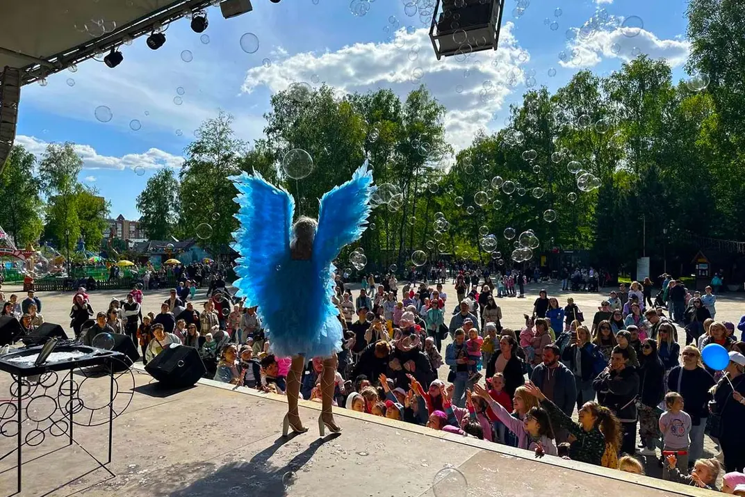 Девушка в голубом костюме ангела выступает на сцене в парке