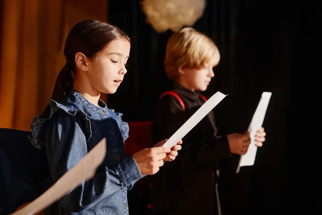 Девочка и мальчик читают текст с листков на сцене театра