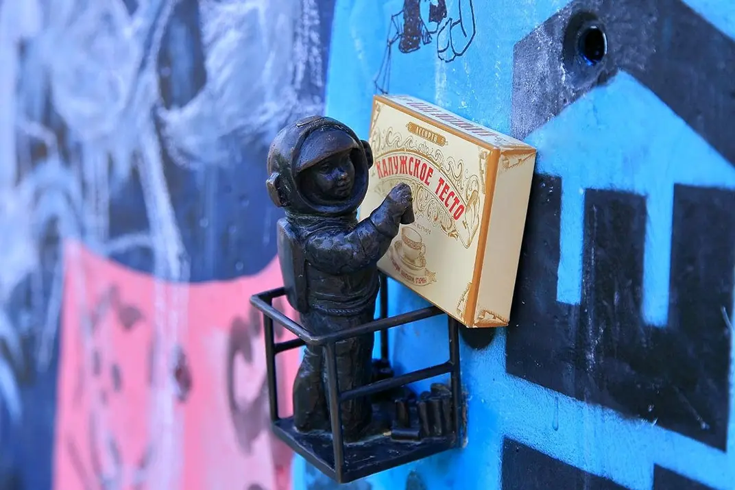 Фигурка космонавтика на подъемнике и упаковка калужского теста напротив расписанной граффити стены